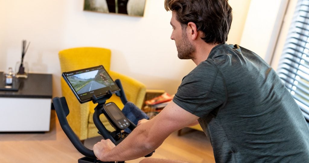 A man follows his indoor cycling workout on his spinning bike