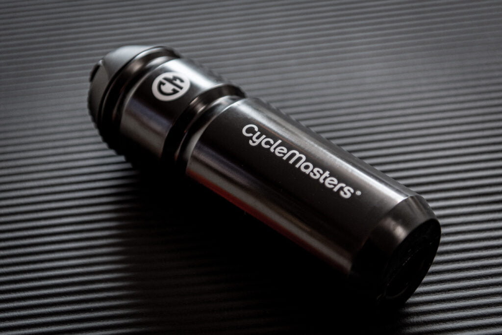 A black and silver cyclemasters branded water bottle lying on a textured dark surface, reflecting light on its body with the logo clearly visible at the top.