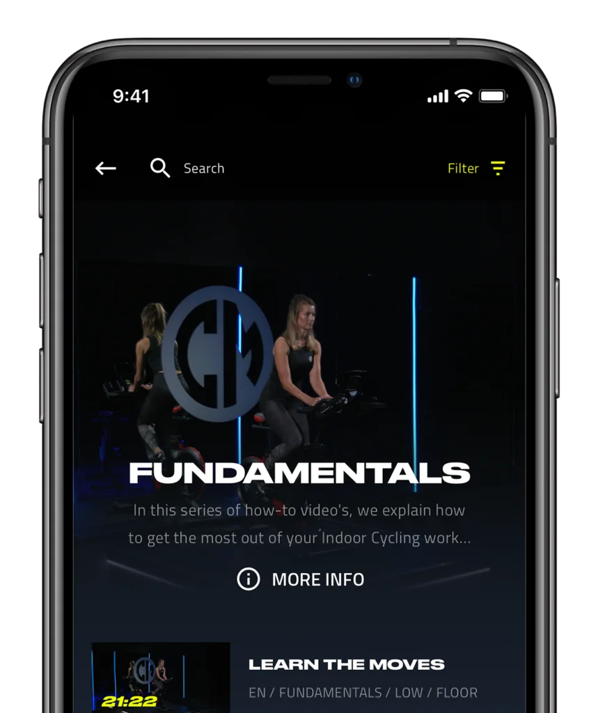 A smartphone screen displaying an indoor cycling workout app, showing a woman on a stationary bike with a "fundamentals" caption and a "learn more" button.