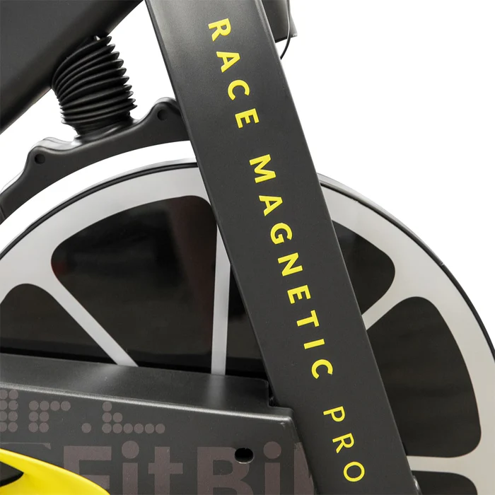Close-up van een onderdeel van een hometrainer met het opschrift 'race Magnetic Pro', waarbij de nadruk ligt op het zwart-gele framedetail bij het vliegwiel.